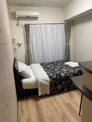 Ett litet, välordnat sovrum med en säng, ett sängbord, ett skrivbord och en luftkonditioneringsanläggning som är monterad på väggen.