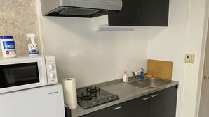 A compact kitchen with a microwave, gas stove, and a sink. - W201 Monthly Rental Tokyo - Large Studio (Setagaya City)