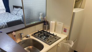 Een kleine keuken met een spoelbak, gasfornuis en een raam met decoratieve roedeindes.