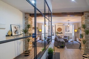 Una sala moderna con sofá, mesa de centro y plantas en macetas. Se ve una escalera con barandillas de vidrio que sube a un nivel superior.