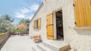 Un edificio con contraventanas de madera, un patio con suelo de piedra y mobiliario exterior.