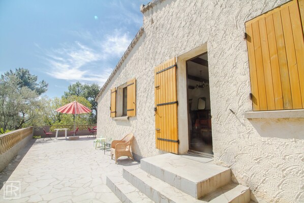 A building with wooden shutters, a patio with stone flooring, and outdoor furniture.
