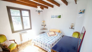 Un dormitorio con cama, dos sillas, una ventana, un radiador y una lámpara colgante.
