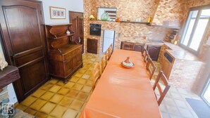 Una cocina con piso de baldosas, armarios de madera, una mesa de comedor con sillas y un ventanal grande.