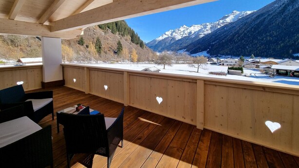 Une terrasse en bois ornée de découpes en forme de cœur, offrant une vue sur un paysage montagneux enneigé.