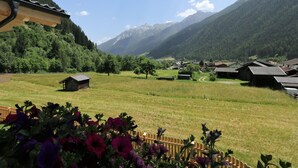 Un paysage rural avec une petite cabane en bois, de vastes champs ouverts et des montagnes en arrière-plan.