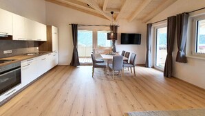 Une cuisine moderne avec des meubles en bois, un coin repas comprenant une table et des chaises, et de grandes fenêtres avec des rideaux.