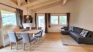 Un vaste espace de vie comprenant une table à manger en bois, des chaises grises, un canapé gris et une grande fenêtre agrémentée de rideaux.