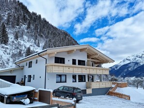A modern two-story chalet with a balcony, a car parked in front, and a snowy mountainous backdrop. - Apartments Alpenpanorama, Neustift (Neustift Im Stubaital)