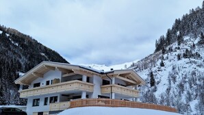 Un chalet à plusieurs étages doté d’un balcon, entouré de montagnes et d’arbres couverts de neige.