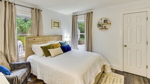 Un dormitorio con cama, una silla, una ventana con cortinas, una puerta y una estantería en la pared.