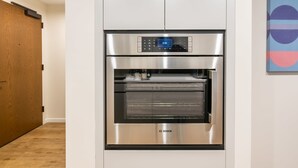 A modern kitchen with a built-in Bosch oven and microwave, a wooden door, and a colorful abstract painting on the wall. - Modern Apt with Gym Near Restaurants (Boston, MA)