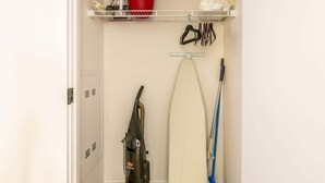 A storage closet with shelves holding a red pot, a white bucket, and cleaning supplies. - Modern Apt with Gym Near Restaurants (Boston, MA)