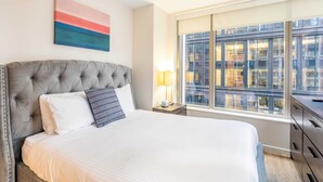 A hotel room with a large bed, a modern headboard, a bedside table with a lamp, and a large window offering a city view. - Modern Apt with Gym Near Restaurants (Boston, MA)