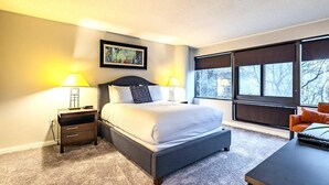 Une chambre d’hôtel moderne avec un grand lit, deux lampes de chevet, un bureau et une fenêtre donnant sur des arbres.