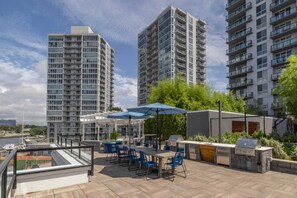 Una terraza en la azotea con mobiliario exterior, una parrilla y vistas de edificios residenciales altos.
