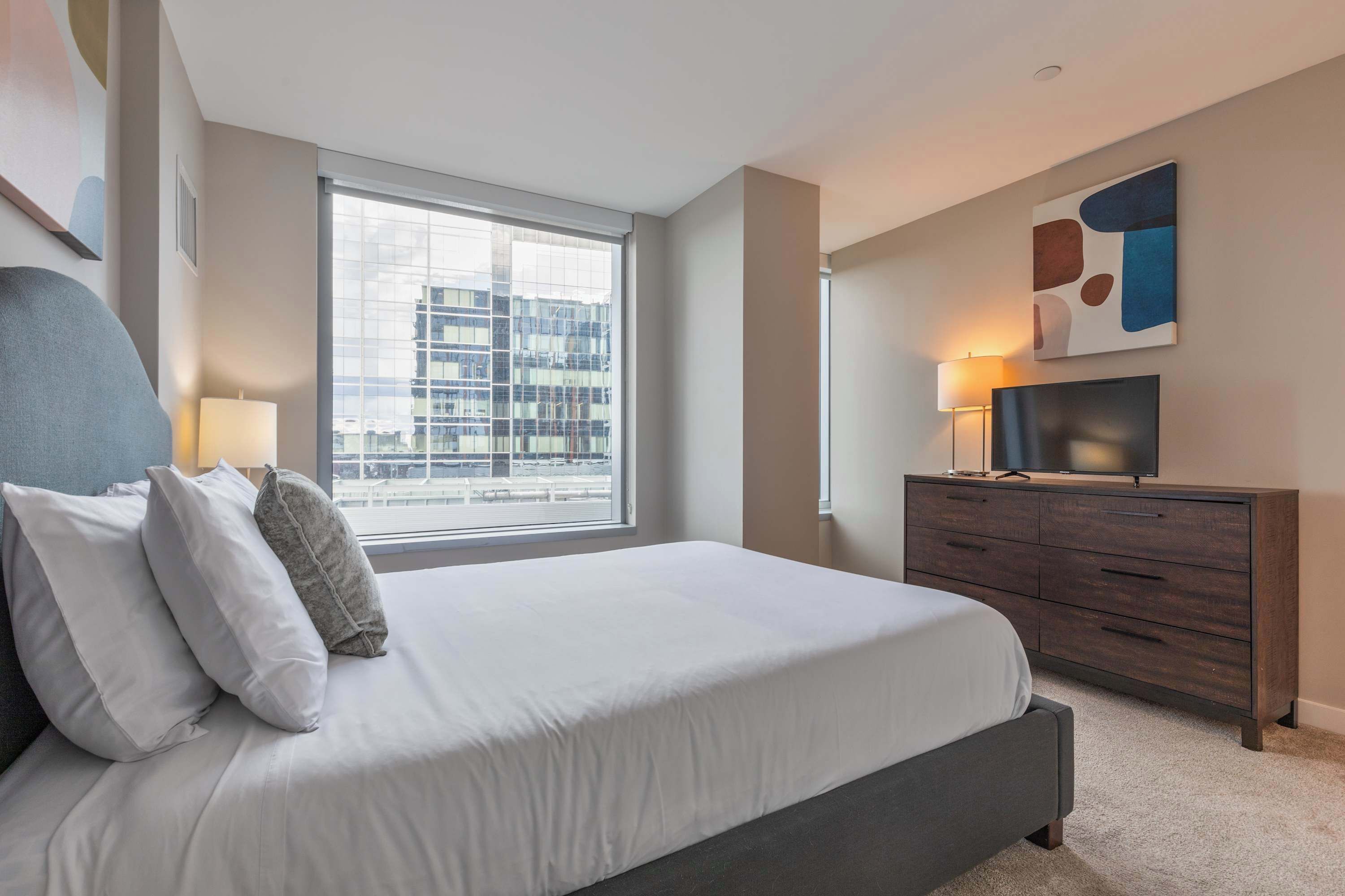 Une chambre d’hôtel moderne dotée d’un grand lit, d’une télévision à écran plat, d’une commode et d’une fenêtre donnant sur la ville.