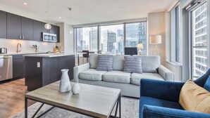 A modern living room with a sofa, a coffee table, and a view of the city through large windows.