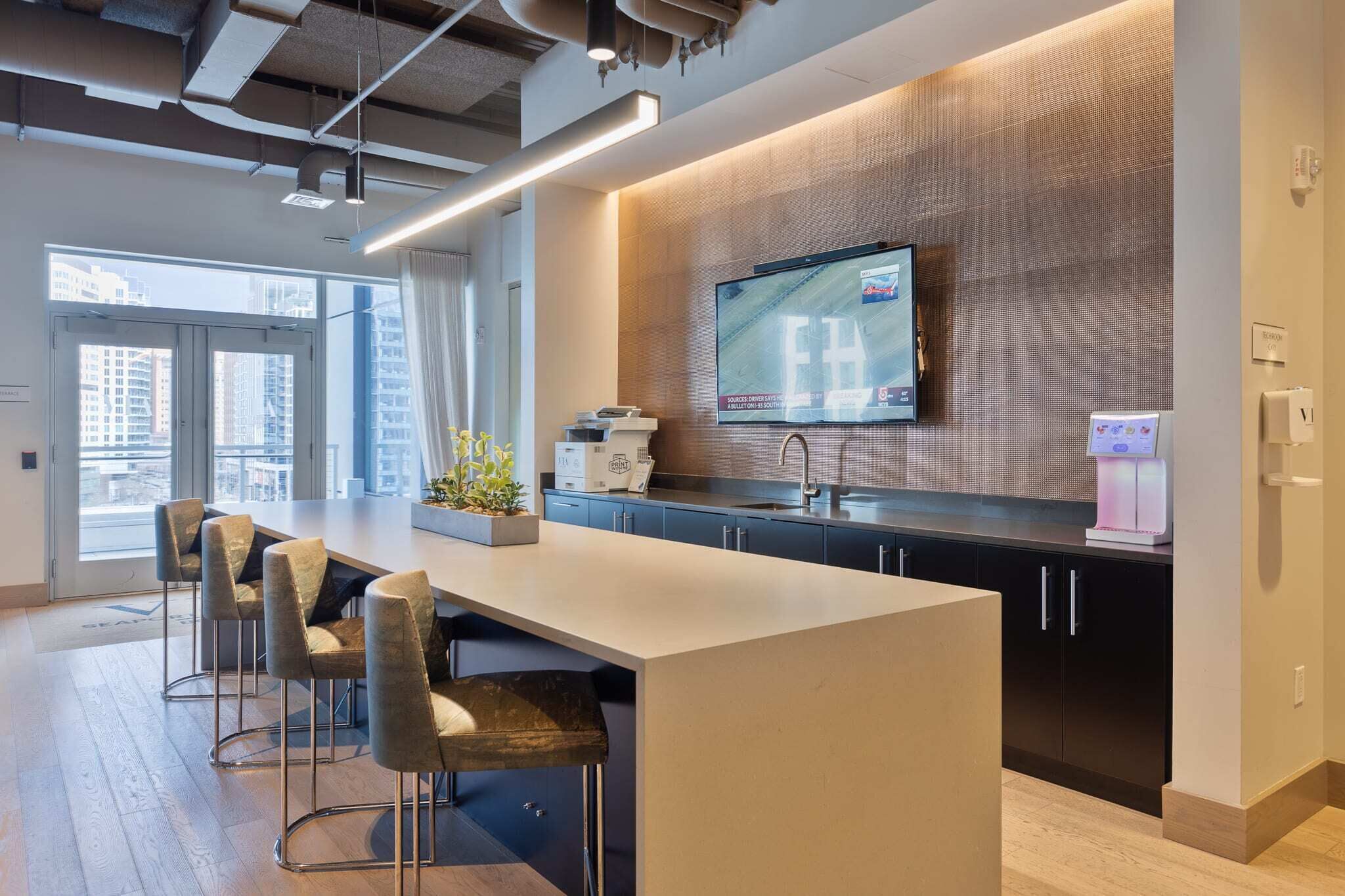A modern kitchen with a large island, bar stools, a flat-screen TV, and a coffee machine.