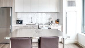 Eine moderne Küche mit weißen Schränken, einem Edelstahlkühlschrank, einer Kaffeemaschine und einem Gasherd.