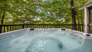 A hot tub surrounded by trees, with a railing and a building in the background.