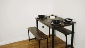 Une petite table à manger avec un banc, un vase blanc et des bols noirs.