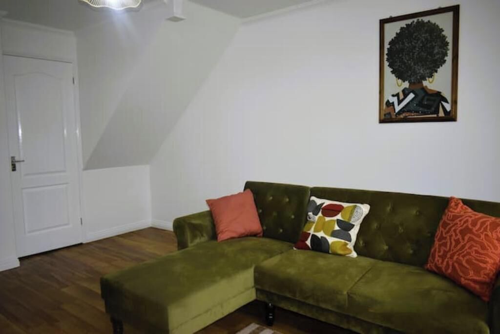 Un sofá verde con un cojín estampado, una almohada roja y una obra de arte enmarcada en la pared.