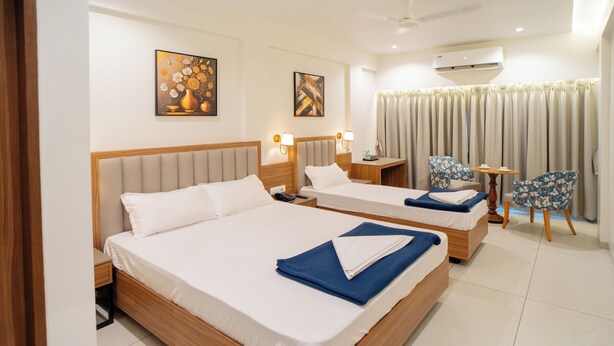 A hotel room with two beds, a desk, a chair, and a small table. - Hotel Anugraha NX (Palghar)