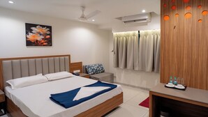 A modern hotel room with a large bed, a bedside table, a nightstand, a wooden wardrobe, a ceiling fan, and a wall-mounted air conditioning unit. - Hotel Anugraha NX (Palghar)