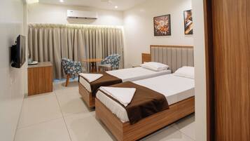 A hotel room with two beds, a television, a small table, a chair, and a window with curtains.
