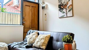 Un salon moderne avec un canapé en cuir, une petite table d’appoint blanche ornée d’une plante et une porte en bois.