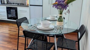 Une cuisine moderne avec des meubles blancs, un réfrigérateur, une cuisinière et un coin repas comprenant une table en verre et des chaises noires.