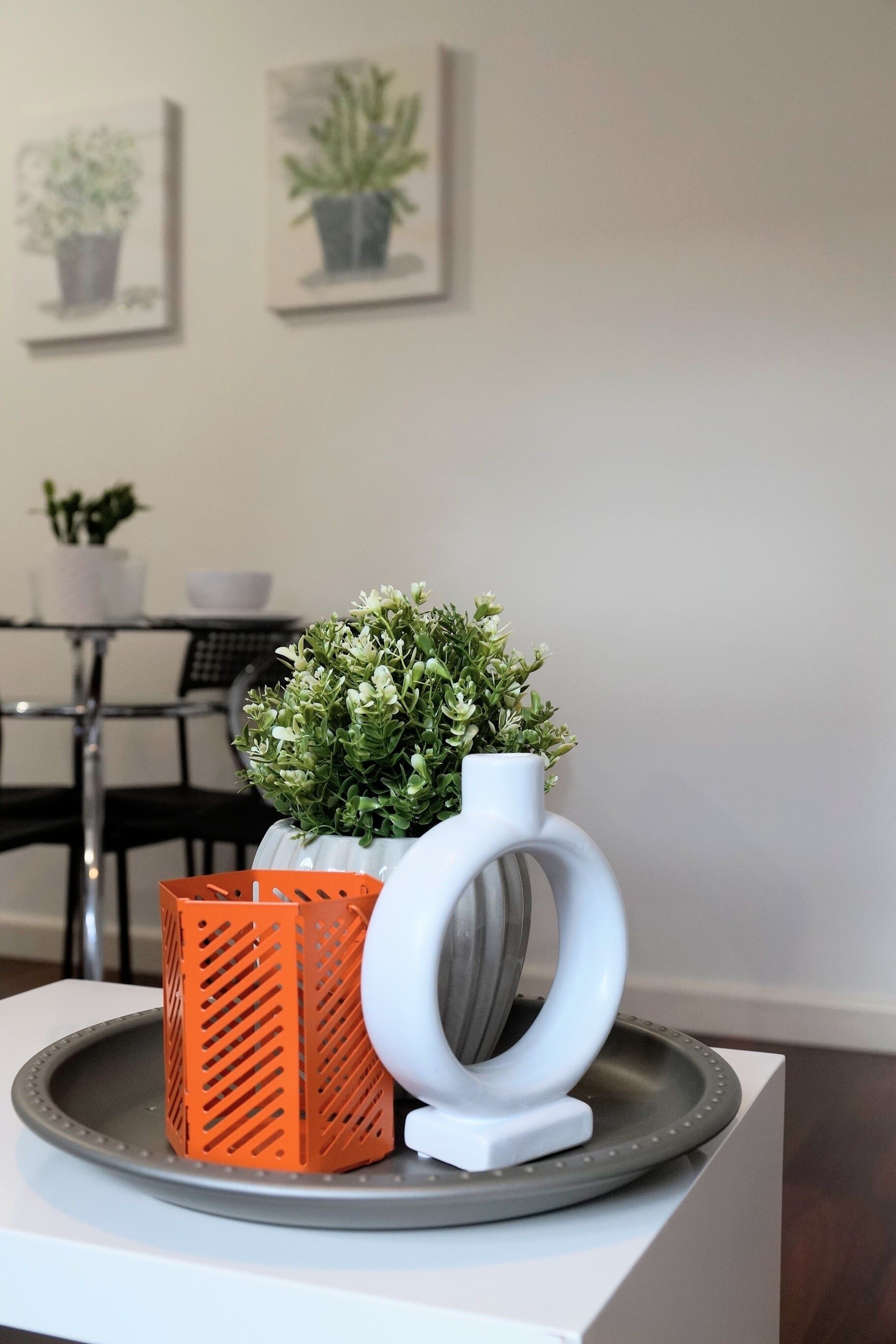 Et spisebord med en potteplante, en hvid vase og en orange kurv på en bakke.