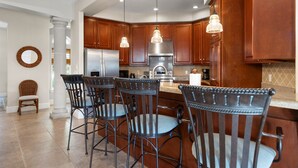 A modern kitchen with wooden cabinets, a stainless steel refrigerator, and a bar area with metal chairs.