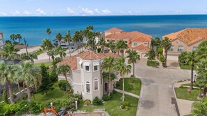 A coastal residential area with houses featuring red-tiled roofs, palm trees, and a clear view of the ocean.
