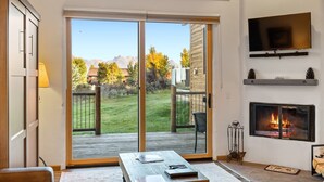 Ein Wohnzimmer mit Kamin, einem an der Wand befestigten Fernseher und einer Glastür zum Balkon.