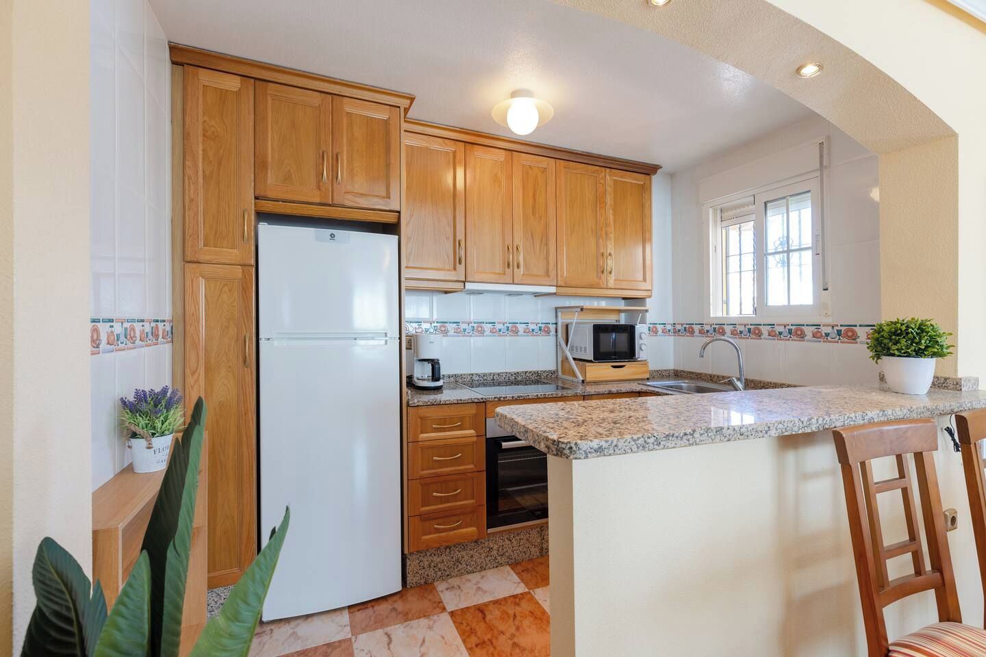 Eine Küche mit Holzschränken, einem Kühlschrank, einer Mikrowelle, einem Spülbecken und einem Blumentopf.