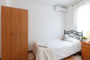 Un dormitorio con un armario de madera, una cama con almohada estampada, una mesita de noche con lámpara y un equipo de aire acondicionado.