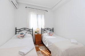 A bedroom with two beds, a nightstand, a lamp, and a window with curtains.