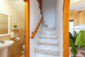 Un baño con lavamanos, inodoro y una escalera de madera que da a una zona de cocina.