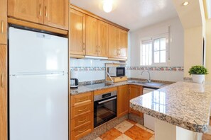 A kitchen with wooden cabinets, a white refrigerator, a microwave, and a sink.