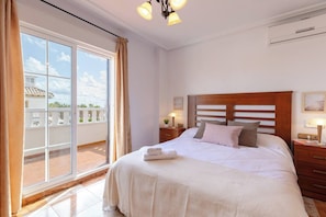 Habitación de hotel con una cama grande, una mesita de noche, una lámpara y vistas al exterior.