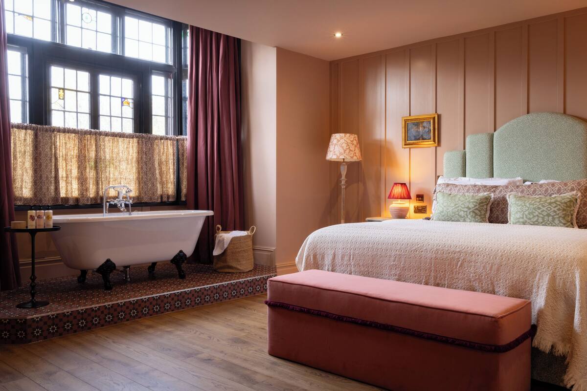 A bedroom with a large bed, a bathtub, and a window with curtains.