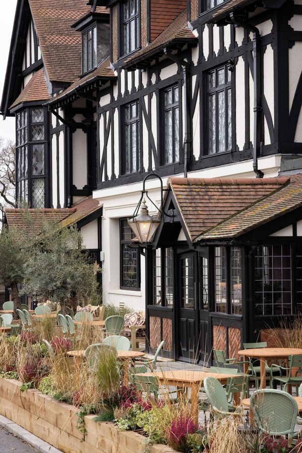 A traditional Tudor-style building with a pub seating area featuring outdoor tables and chairs.