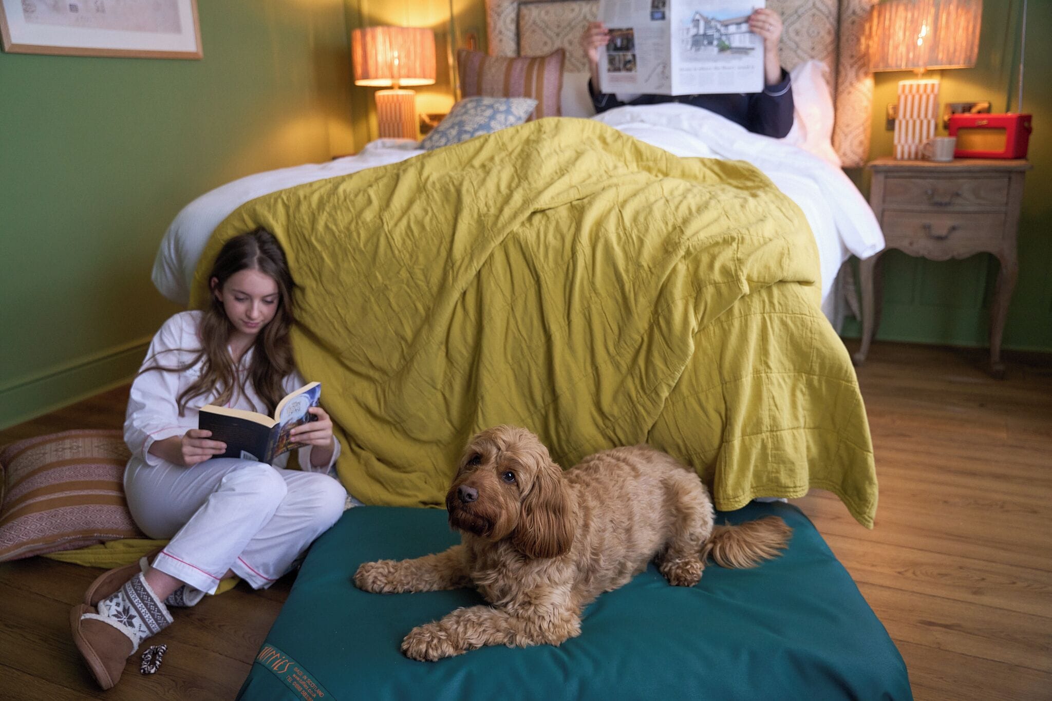 A person reading a book on a bed with a dog lying beside them.