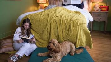 A person reading a book on a bed with a dog lying beside them.