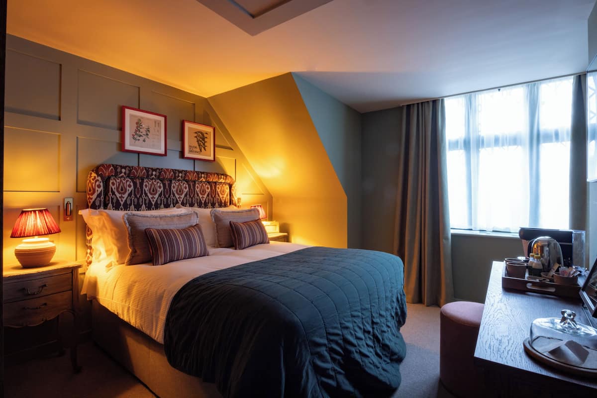 A hotel room with a bed, bedside lamps, a desk with a chair, and a window with curtains.