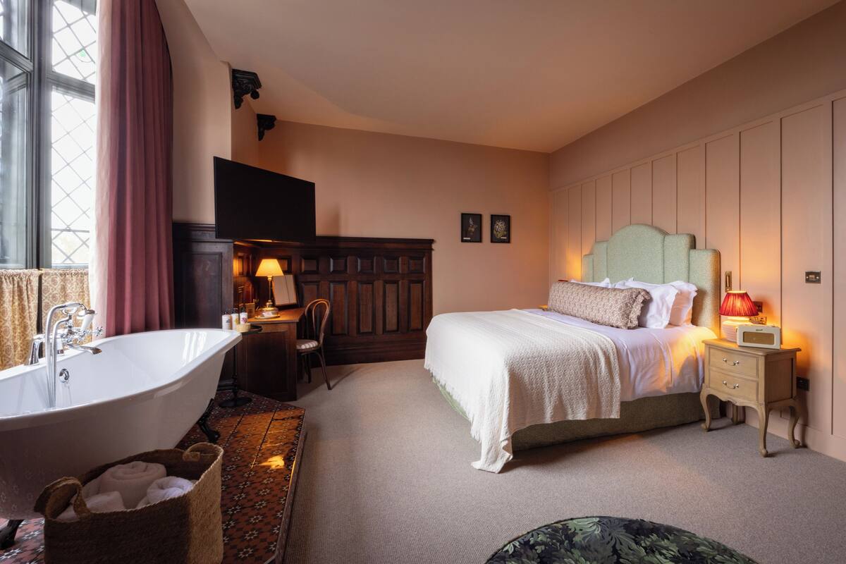 A bedroom with a large bed, a sitting area with a desk and chair, a bathtub, and a wardrobe.