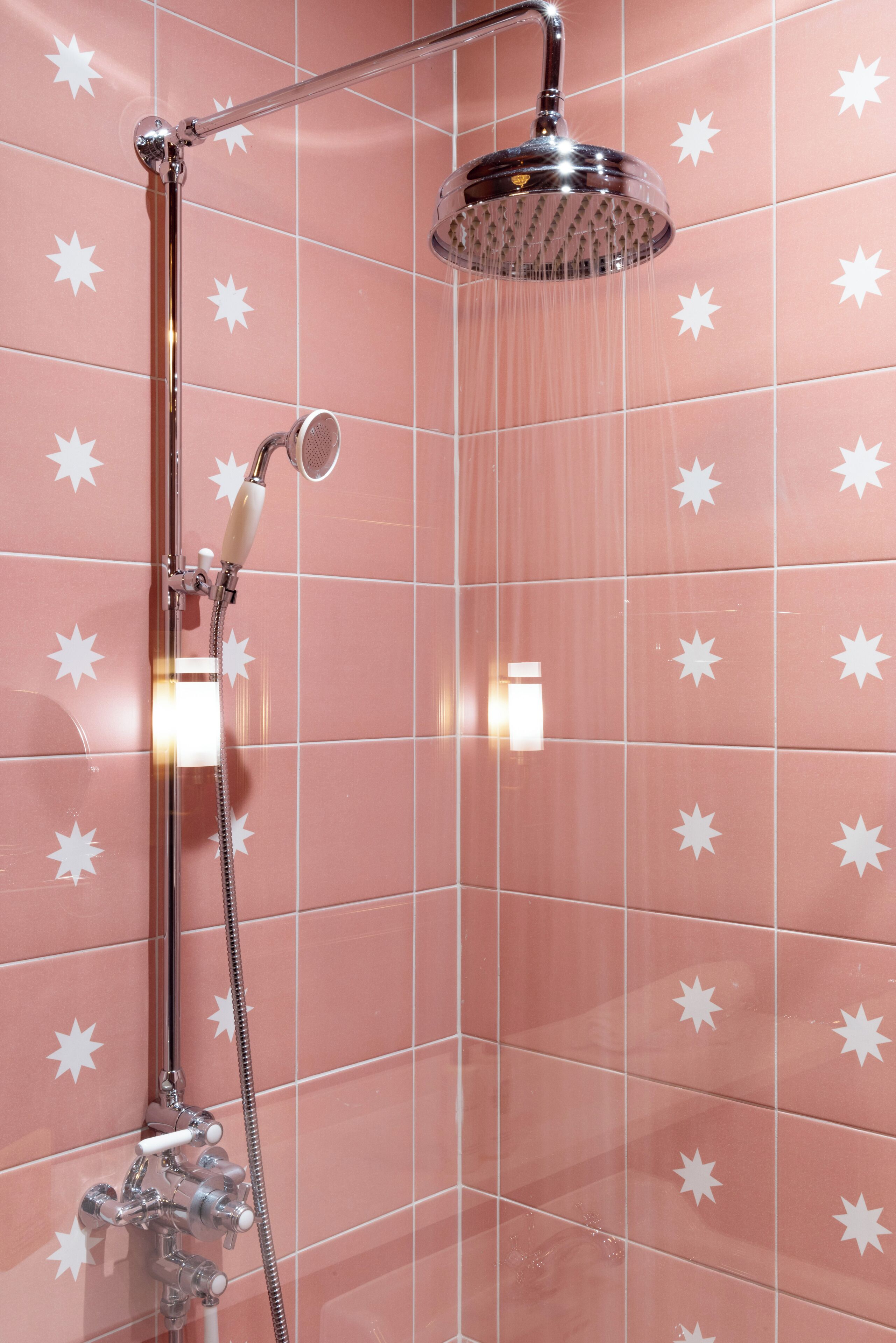A shower with a handheld showerhead and a wall-mounted rain showerhead, set against pink tiles with white star patterns.