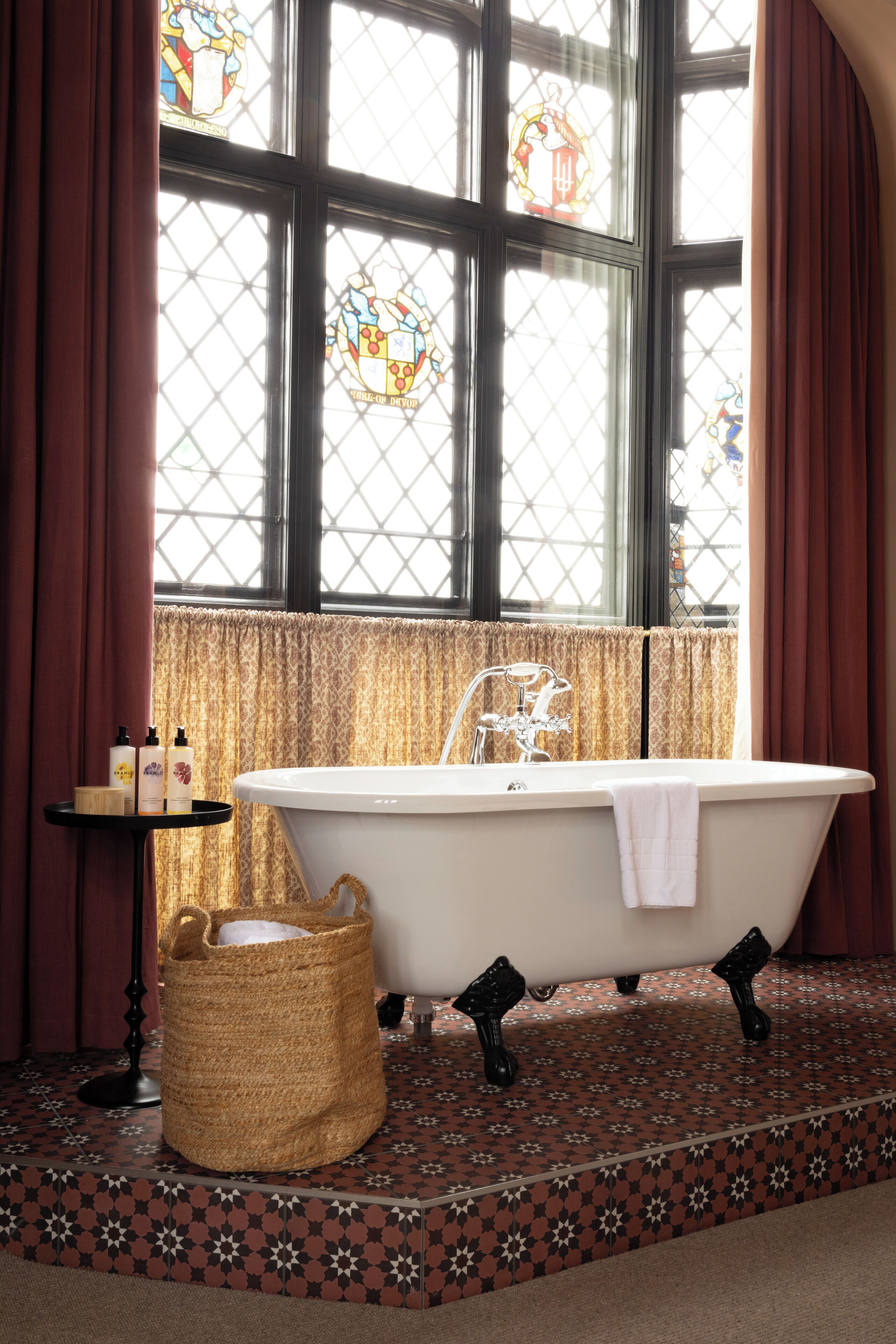 A bathroom with a freestanding bathtub, a wicker basket, and a small table with toiletries.